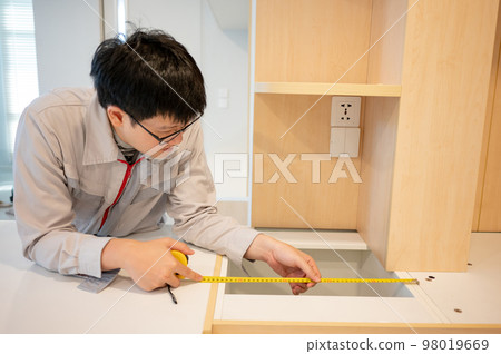 Asian male furniture assembler using tape measure Asian male furniture assembler using tape measure 98019669