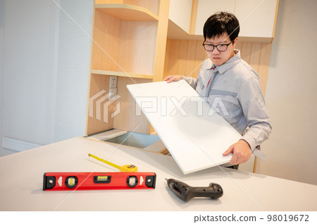 Asian male furniture assembler installing cabinet panel Asian male furniture assembler installing cabinet panel 98019672