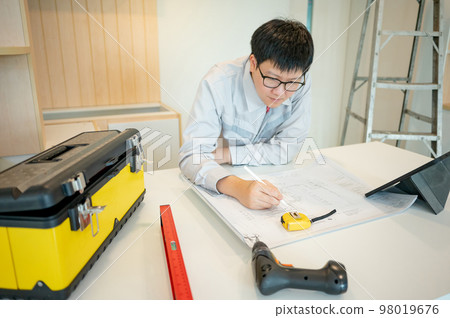 Asian male Interior worker working with architectural drawing 98019676