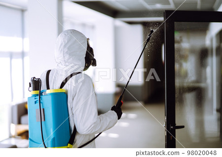 Disinfecting of office to prevent COVID-19, Man in protective hazmat suit with spray chemicals. 98020048