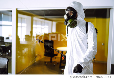 Disinfecting of office to prevent COVID-19, Man in protective hazmat suit with spray chemicals. Disinfecting of office to prevent COVID-19, Man in protective hazmat suit with spray chemicals. 98020054