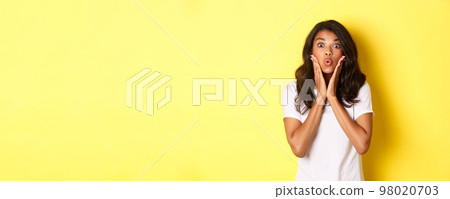 Portrait of attractive african-american teenage girl looking amazed, saying wow and stare at camera excited, standing over white background Portrait of attractive african-american teenage girl looking amazed, saying wow and stare at camera excited, standing over white background 98020703