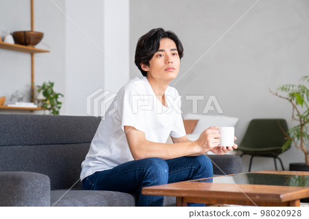 Young man drinking coffee in the living room Young man drinking coffee in the living room 98020928