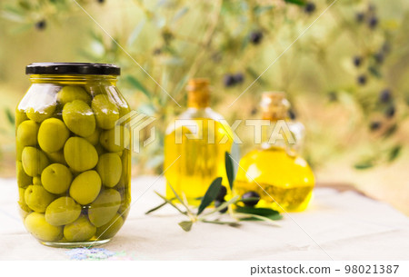 canned olives in a glass jar, oil and olives on the table against the background of the olive garden canned olives in a glass jar, oil and olives on the table against the background of the olive garden 98021387