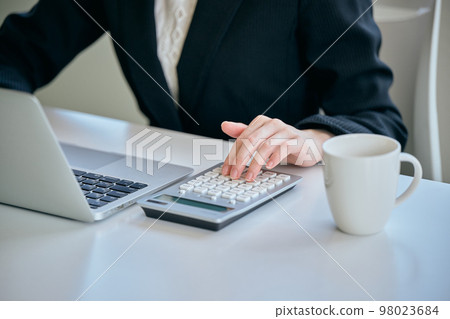 Young woman doing calculations with a calculator in the office 98023684