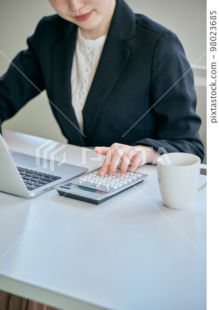 Young woman doing calculations with a calculator in the office 98023685