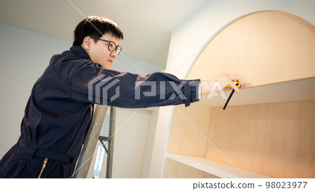 Asian male furniture assembler using tape measure Asian male furniture assembler using tape measure 98023977