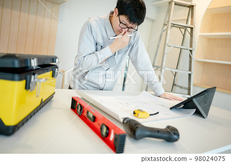 Asian male Interior worker working with architectural drawing Asian male Interior worker working with architectural drawing 98024075