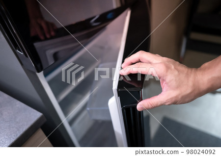 Male hand opening fridge or refrigerator door in kitchen 98024092