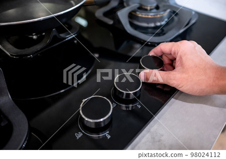 Male hand turning switch knob on gas stove Male hand turning switch knob on gas stove 98024112