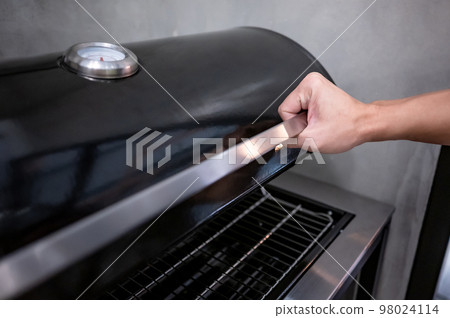 Male hand opening outdoor gas barbecue (BBQ) grill Male hand opening outdoor gas barbecue (BBQ) grill 98024114