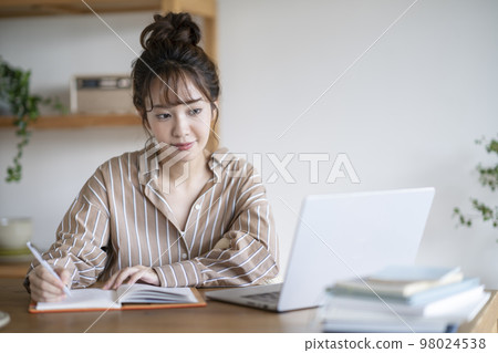 Young woman taking notes while looking at laptop screen 98024538