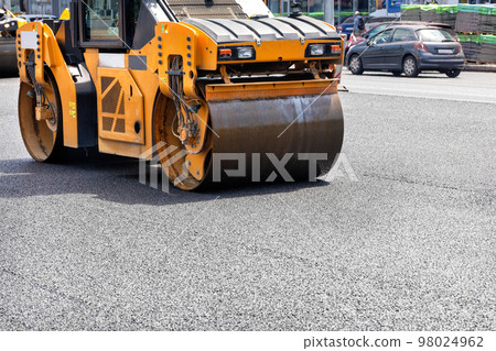 The vibrating roller rams and compacts the fresh asphalt in the middle of the carriageway on the road. The vibrating roller rams and compacts the fresh asphalt in the middle of the carriageway on the road. 98024962