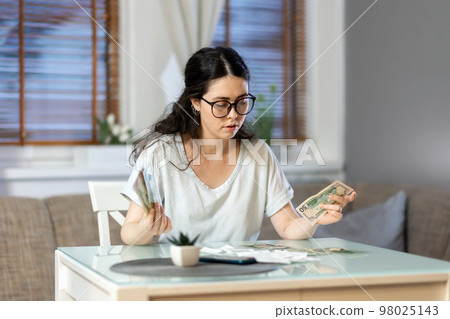 Planning of expenses. Portrait of caucasian young woman accounting cash and paper receipt. Concept of payment of utilities, tax return and savings Planning of expenses. Portrait of caucasian young woman accounting cash and paper receipt. Concept of payment of utilities, tax return and savings 98025143