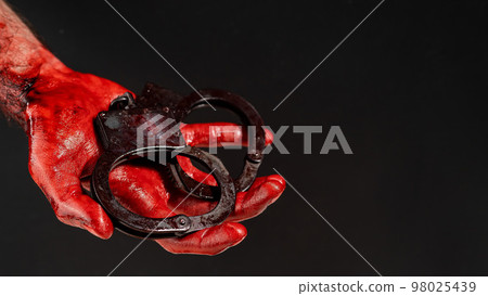 Faceless man holding handcuffs black background. Hands are stained with blood. 98025439