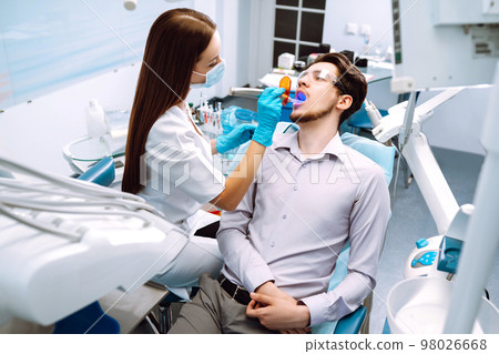Young man at the dentist's chair during a dental procedure. Overview of dental caries prevention. 98026668
