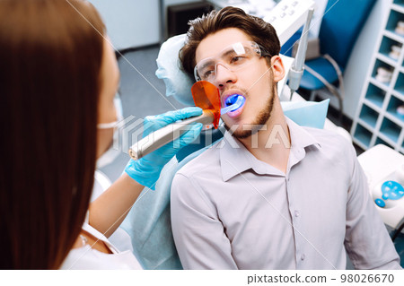 Young man at the dentist's chair during a dental procedure. Overview of dental caries prevention. Young man at the dentist's chair during a dental procedure. Overview of dental caries prevention. 98026670