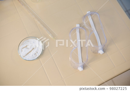 Top view - protective goggles near Petri dish with white powder, on a plastic table in the scientific chemistry and biology laboratory 98027225
