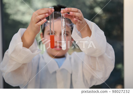 Details: test tubes with chemicals in the hands of blurred schoolboy, chemist scientist in white lab coat, examining features of substances inside test tubes, conducting experiments at chemistry class 98027232