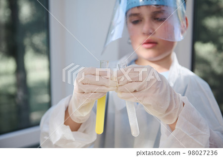 Details: gloved hands of a blurred smart teen schoolboy, wearing protective lab wear, holding test tubes with chemicals and reagents, conducting experiment in the school chemistry laboratory 98027236