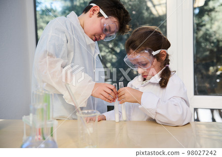 Concentrated Caucasian smart kids conducting chemical experiment, watching the reaction taking place in test tubes in the school laboratory during Chemistry class. Education. Back to school concept Concentrated Caucasian smart kids conducting chemical experiment, watching the reaction taking place in test tubes in the school laboratory during Chemistry class. Education. Back to school concept 98027242