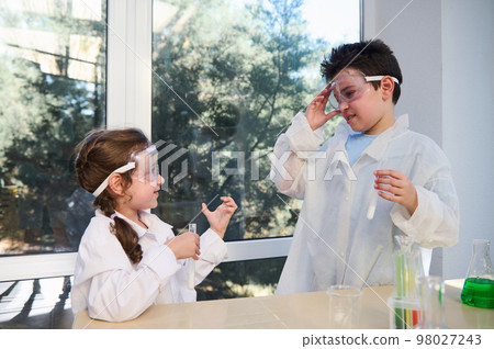 Adorable Caucasian diverse kids enjoying chemistry lesson in a school laboratory. School Children wearing white lab coats and safety goggles, conducting chemical experiments. Back to school concept Adorable Caucasian diverse kids enjoying chemistry lesson in a school laboratory. School Children wearing white lab coats and safety goggles, conducting chemical experiments. Back to school concept 98027243