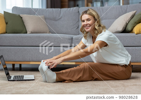 Portrait of active woman at home doing fitness and exercise and yoga, mature housewife looking at camera and smiling using laptop for online fitness training with trainer. 98028628