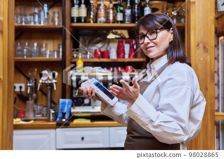 Woman worker manager of restaurant holding wireless banuov payment terminal Woman worker manager of restaurant holding wireless banuov payment terminal 98028865