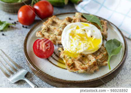 Spinach and zucchini vegan waffles with a poached egg on a stone tabletop. The concept of dietary and healthy breakfast. Spinach and zucchini vegan waffles with a poached egg on a stone tabletop. The concept of dietary and healthy breakfast. 98028892