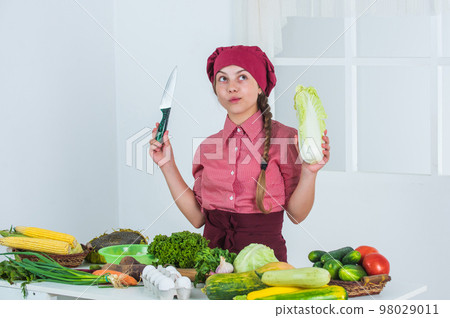 what to cook. full of vitamins. kid wear chef uniform and hat. teen girl preparing chinese cabbage. fresh raw vegetables. time to eat. happy child cooking in kitchen. healthy and organic food only what to cook. full of vitamins. kid wear chef uniform and hat. teen girl preparing chinese cabbage. fresh raw vegetables. time to eat. happy child cooking in kitchen. healthy and organic food only 98029011