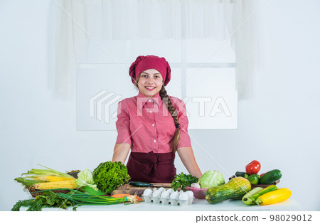 happy kid girl in cook hat and apron in kitchen, dieting happy kid girl in cook hat and apron in kitchen, dieting 98029012