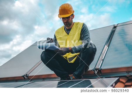 Man works on renewable energy system with solar panel for electricity and hot water Man works on renewable energy system with solar panel for electricity and hot water 98029340