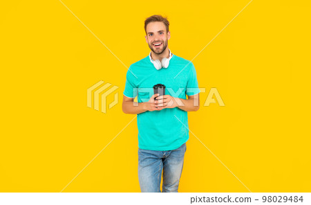 smiling unshaven young man in headphones drink coffee on yellow background, technology smiling unshaven young man in headphones drink coffee on yellow background, technology 98029484