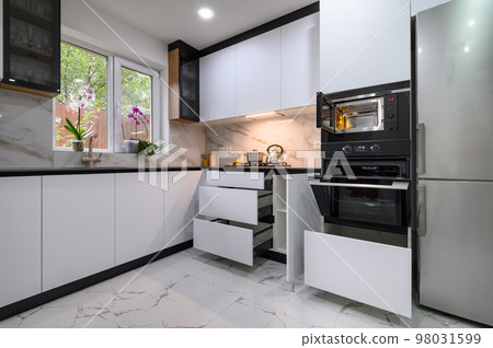A contemporary kitchen with white cabinets, a marble floor, an open oven door, and pull-out shelves A contemporary kitchen with white cabinets, a marble floor, an open oven door, and pull-out shelves 98031599
