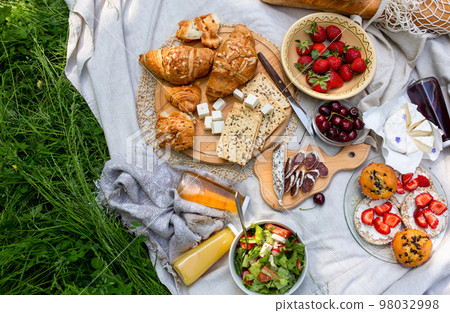 Picnic in the field with berries, juice, cheese, sausage and sweet croissants 98032998