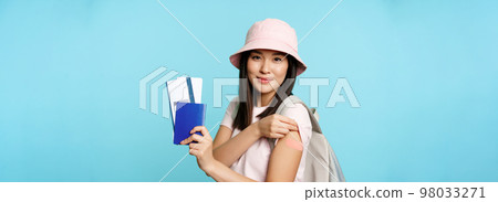 Happy asian girl tourist got vaccinated to travel abroad, showing arm with plaster and passport with two tickets, booking tour, travelling during pandemic, blue background Happy asian girl tourist got vaccinated to travel abroad, showing arm with plaster and passport with two tickets, booking tour, travelling during pandemic, blue background 98033271