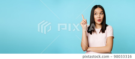 Eureka. Young asian woman found solution. Korean girl raising finger up and pitching an idea, standing thoughtful over blue background 98033316