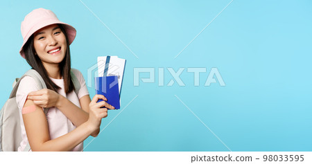 Smiling asian woman shows her passport and flight tickets, covid-19 vaccinated arm with patch, vaccinating to travel abroad, tourism and pandemic concept 98033595