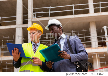 Head of construction and representative of developer are discussing documents and drawings at construction site 98033629