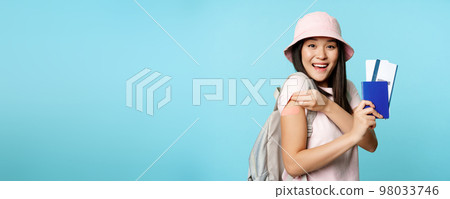 Enthusiastic korean woman shows her vaccinated arm, passport tickets. Tourist looks happy after covid-19 vaccine shot, travelling abroad, tourism concept Enthusiastic korean woman shows her vaccinated arm, passport tickets. Tourist looks happy after covid-19 vaccine shot, travelling abroad, tourism concept 98033746