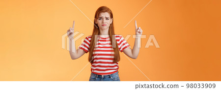 Disappointed upset cute whining timid redhead girl, gloomy face, pulling sad expression, complain, crying feeling regret loss, losing lottery, pointing up displeased, show despair and sorrow emotion 98033909