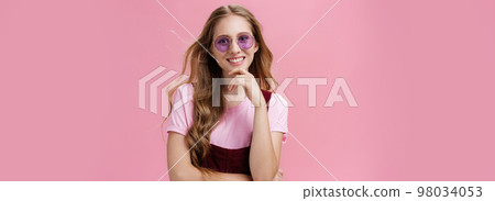 Beauty, style and fashion concept. Portrait of charming confident european female with natural wavy hair in sunglasses and overalls touching chin amused and smiling broadly against pink wall Beauty, style and fashion concept. Portrait of charming confident european female with natural wavy hair in sunglasses and overalls touching chin amused and smiling broadly against pink wall 98034053