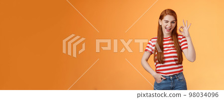 Sassy stylish sly redhead cheerful girl assuring everything excellent, show okay sign and wink cheeky, accept awesome idea, approve good job, express satifaction from positive result, like choice 98034096