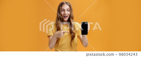 Portrait of excited woman feeling amazed holding awesome new smartphone in hand pointing at cellphone screen popping eyes like crazy at device being charmed with cool technology product 98034243