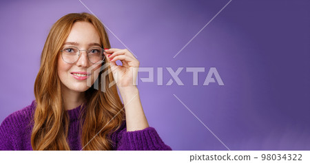 Cute nerdy female student with natural beautiful red hair touching rim of glasses and smiling promising and self-assured at camera eager see what future holds after graduation over purple background Cute nerdy female student with natural beautiful red hair touching rim of glasses and smiling promising and self-assured at camera eager see what future holds after graduation over purple background 98034322
