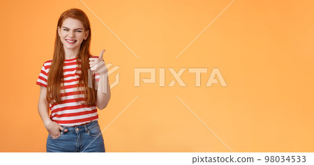 Cheerful friendly woman red natural hair clean skin, show thumb up, smiling approval, support perfect choice, like excellent performance, express positive opinion, acceptance, orange background 98034533