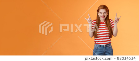 Rebellious sassy good-looking caucasian redhead woman partying having fun, enjoy awesome stunning concert, favorite band, raise heavy-metal signs entertained, smiling sly squinting joyful 98034534