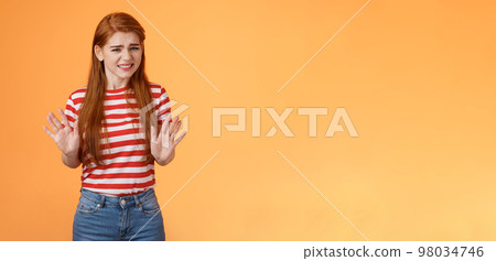 Reluctant bothered cute redhead girl apologizing make stop refusal sign, hold hands block, grimacing, cringe unwilling participate, rejecting offer, stand orange background uncomfortable, step back 98034746