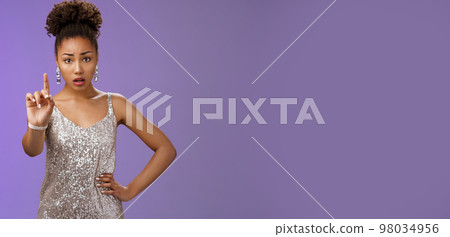 Concerned worried young african-american woman in trendy dress extend index finger nervously look camera shushing prohibiting tell anyone secret frowning afraid, saying taboo, blue background 98034956