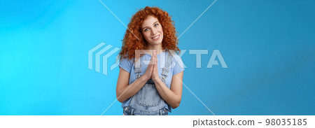Girl acting like nun redhead cute curly female press palms together pray supplication gesture tilting head silly smiling innocent angel gaze pleading begging favour asking something blue background 98035185